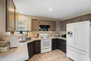 Kitchen featuring white appliances, light countertops, light tile patterned floors, recessed lighting, and dark brown cabinetry
