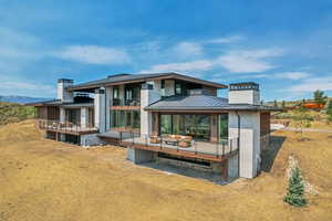 Rear view of house featuring a standing seam roof, a metal roof, a deck, a balcony, and a chimney