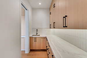 Bar with light brown cabinets, light stone countertops, light wood finished floors, modern cabinets, and decorative backsplash