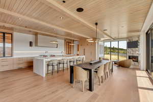 Dining space with light wood-style flooring, a wooden ceiling with exposed beams, floor to ceiling windows, and a fireplace