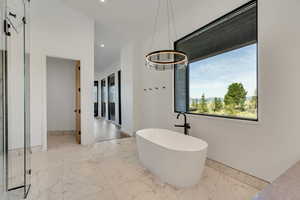 Full bathroom with light marble finish floors, a soaking tub, recessed lighting, and a chandelier