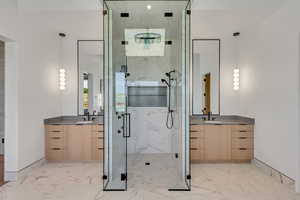 Full bath featuring light marble finish floors, a marble finish shower, and two vanities