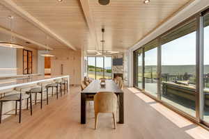 Dining space featuring light wood finished floors, a fireplace, and a wooden ceiling with exposed beams