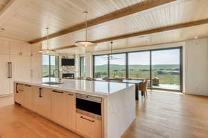 Kitchen featuring beamed ceiling, light brown cabinets, hanging light fixtures, light wood-style floors, and light stone counters