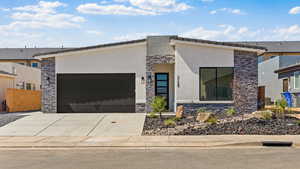 Contemporary house featuring stone siding, stucco siding, a garage, and concrete driveway