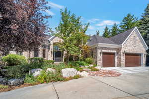 View of property hidden behind natural elements with a shingled roof, an attached garage, driveway, and brick siding