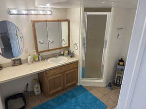 Full bathroom featuring light tile patterned floors, a stall shower, vanity, and a textured ceiling