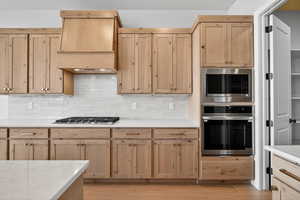 Kitchen with light brown cabinetry, stainless steel appliances, decorative backsplash, and light stone countertops