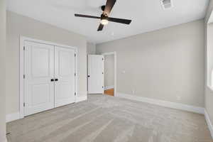 Unfurnished bedroom with light colored carpet, a ceiling fan, and a closet