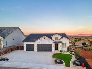 Modern inspired farmhouse with an attached garage, driveway, stone siding, and board and batten siding