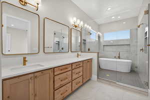 Full bathroom featuring double vanity, a stall shower, a freestanding tub, light marble finish floors, and recessed lighting