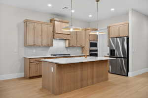 Kitchen featuring stainless steel appliances, tasteful backsplash, hanging light fixtures, light stone countertops, and light brown cabinetry