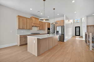 Kitchen featuring light brown cabinetry, decorative backsplash, an island with sink, stainless steel fridge with ice dispenser, and a chandelier