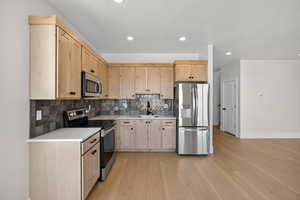 Kitchen featuring light brown cabinets, appliances with stainless steel finishes, decorative backsplash, light wood finished floors, and recessed lighting