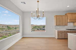 Kitchen featuring hanging light fixtures, a chandelier, light brown cabinetry, light wood-type flooring, and tasteful backsplash