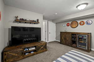 Living room featuring a textured ceiling, carpet floors, wine cooler, and bar