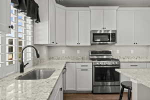 Kitchen with stainless steel appliances, light stone counters, white cabinets, and dark wood-type flooring