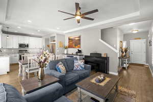 Living area featuring light wood finished floors, a tray ceiling, ceiling fan, and recessed lighting