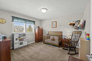 Bedroom featuring a nursery area, carpet, and a textured ceiling