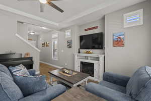 Living area with a glass covered fireplace, wood finished floors, and a ceiling fan