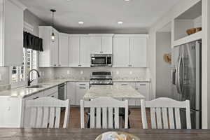 Kitchen with appliances with stainless steel finishes, white cabinets, hanging light fixtures, light stone countertops, and recessed lighting