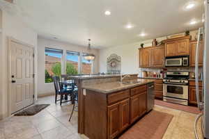 Kitchen with a kitchen breakfast bar, a kitchen island with sink, light tile patterned floors, brown cabinetry, and stainless steel appliances
