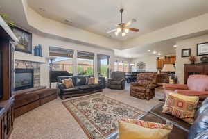 Living area with carpet floors, a tray ceiling, a fireplace, recessed lighting, and ceiling fan