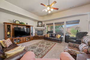 Carpeted living area with a fireplace and ceiling fan
