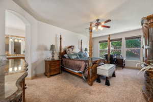 Bedroom with light carpet, arched walkways, and ceiling fan