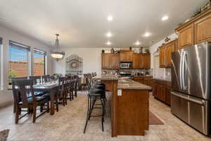 Kitchen with stainless steel appliances, decorative backsplash, brown cabinets, a breakfast bar area, and recessed lighting