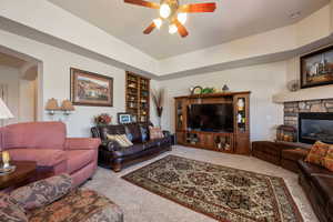 Carpeted living room with ceiling fan, a raised ceiling, and a fireplace