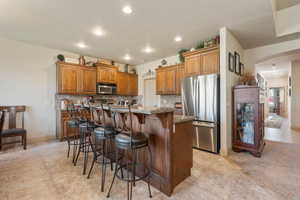 Kitchen with a breakfast bar, stainless steel appliances, backsplash, brown cabinets, and recessed lighting
