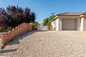 View of side of home with a gate, stucco siding, driveway, an attached garage, and a tile roof