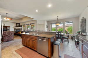 Kitchen featuring brown cabinets, stainless steel appliances, a fireplace, dark stone countertops, and an island with sink