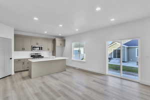 Kitchen featuring recessed lighting, an island with sink, stainless steel appliances, light wood-type flooring, and light stone countertops