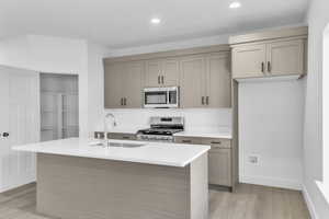 Kitchen featuring stainless steel appliances, light wood-type flooring, light stone counters, an island with sink, and recessed lighting