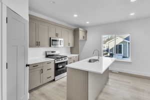 Kitchen with appliances with stainless steel finishes, recessed lighting, a center island with sink, light wood-style floors, and light stone countertops