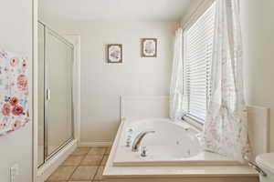 Bathroom with a stall shower, light tile patterned floors, and a jetted tub