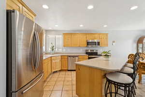 Kitchen featuring appliances with stainless steel finishes, recessed lighting, light brown cabinetry, light tile patterned flooring, and a breakfast bar area