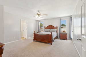 Primary bedroom featuring light carpet and a ceiling fan with private bathroom