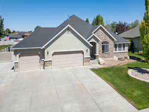 View of front facade with stone siding, roof with shingles, driveway, and a garage