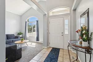 Entryway with light tile patterned floors, light carpet, and high vaulted ceiling