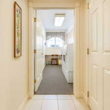 Corridor featuring light carpet, light tile patterned floors, and washing machine and dryer