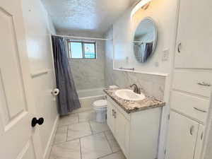 Full bathroom featuring shower / bath combination with curtain, vanity, a textured ceiling, light marble finish floors, and tile walls