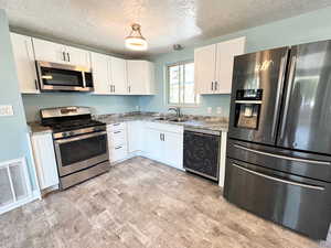 Kitchen with appliances with stainless steel finishes, a textured ceiling, white cabinets, light wood-style flooring, and decorative light fixtures