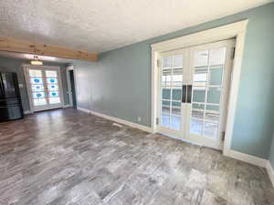 Unfurnished living room with french doors, healthy amount of natural light, wood finished floors, a textured ceiling, and beamed ceiling