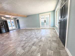 Unfurnished living room featuring french doors, healthy amount of natural light, a textured ceiling, wood finished floors, and beamed ceiling
