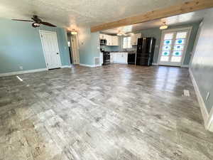 Unfurnished living room with a textured ceiling, french doors, a ceiling fan, wood finished floors, and beamed ceiling