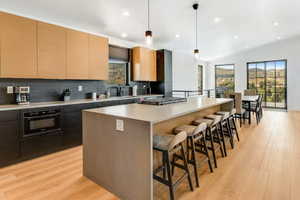 Kitchen featuring tasteful backsplash, a breakfast bar, modern cabinets, a spacious island, and light wood-style flooring