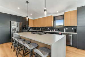 Kitchen featuring light wood finished floors, pendant lighting, stainless steel appliances, a breakfast bar area, and lofted ceiling
